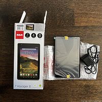 RCA 7 inch Voyager II tablet with original box, bubble wrap, and charger on wooden surface.