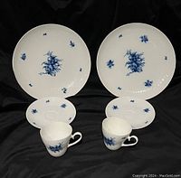 Front view of two plates, two cups, and two saucers set with blue floral pattern on white porcelain.