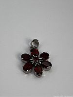 Front view of flower-shaped sterling silver pendant with six red stones and one center red stone.