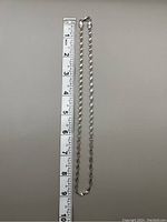 Silver tone twisted chain necklace laid flat next to a ruler showing length about 8 inches.