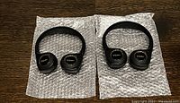Two new black wireless Cadillac headphones placed on bubble wrap on wooden surface, showing Cadillac logos and cushioned ear pads.