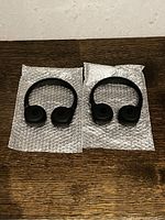 Photo shows two identical black behind-the-neck style in-car headphones placed side by side on bubble wrap on a wooden surface.