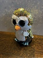 Front and side view of the Ty sequined penguin plush toy showing its large black eyes, orange beak, white face and belly, and reversible sequins covering its body.