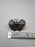 Front view of the vintage filigree butterfly brooch with a ruler for size reference, showing intricate silver tone detailing and a wingspan of about 2 inches.