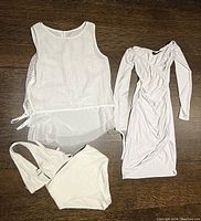 Photo showing Oak and Fort white two-piece bathing suit including a crochet-style sleeveless top with side ties and sheer underlayer, matching bikini bottoms, and a white fitted long-sleeve dress with side splits and v-neck.