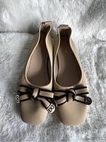 Top view of the pair of new tan women's shoes showing black bow detail on rounded square toe with metal tips bearing 'DD'.