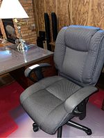 Ergonomic office chair and brass desk lamp on a table with a red carpet and wood paneled wall background