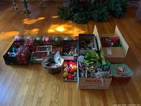 Wide shot showing boxes of Christmas ornaments, ribbons, bows, wrapping paper and basket on hardwood floor.
