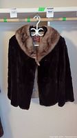 Full view of the dark brown mink jacket with lighter mink fur collar hanging on a hanger