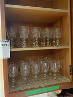 Two shelves of clear crystal juice size glasses with pinwheel pattern etched on bowls, faceted stems and round bases.
