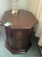 Full view of the octagonal wooden end table showing the side with the storage door and metal ring handle.
