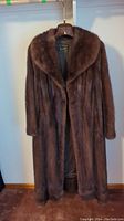 Full view of brown mink fur coat hanging on wooden hanger showing length and large collar.