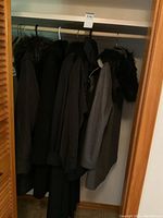 Closet view of six ladies coats hanging on a rack including a grey one with fur collar and darker coats along the back of the closet