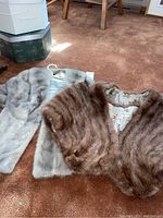 Brown and silver mink stoles laid flat on carpet showing fur texture and form.