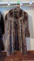Full front view of the racoon fur coat hanging on a rack showing its length and pattern.