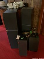 Five JBL speakers of varying sizes with coiled speaker wire on red carpet