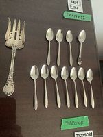 Overview of 10 coffee spoons, 1 souvenir spoon, and 1 cold meat fork on wooden surface