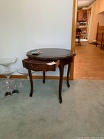 Full view of the round wooden accent table showing drawer and curved legs.