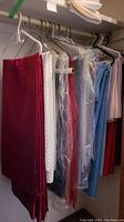 Various tablecloths and napkins hanging on hangers in closet. Colors include dark red, white, clear red, light blue, and pink.