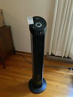 Full height view of black and silver tower fan on hardwood floor.