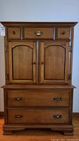 Front view of highboy dresser showing upper small drawers, cabinet doors and lower drawers with brass hardware.