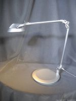 Full view of silver Humanscale Element Vision LED task lamp standing upright on circular base