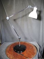 Full view of articulated chrome table lamp showing white shade and black base