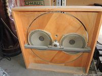 Front view of wooden baffle showing dual 8-inch speakers behind circular cut-out