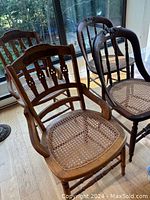 Four antique wooden cane chairs grouped near a window on wood floor showing carved backs and cane woven seats.