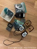 Photo of two Lunasix light meters with brown leather cases alongside two camera flashes and additional camera accessory parts on a wooden floor.