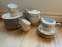 Photo showing entire tea set including stacked saucers, teacups, teapot and creamer on wooden floor