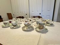 Wide angle view of 21 fine china teacups and matching saucers arranged on a table showing variety of floral patterns and styles.