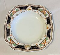 Scalloped edge plate with detailed Art Deco pattern in dark blue, orange, green and gold. Features floral and geometric motifs with gilded accents.