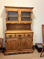 Closed view of two piece solid wood china cabinet with hutch on top and sideboard below, showing wood finish and hardware