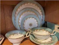 Stacked dinner, salad and dessert plates with matching cups and saucers showing pale green and gold acanthus leaf motif