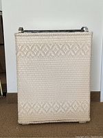 Front view of vintage cream color wicker laundry hamper showing woven decorative pattern and rectangular shape