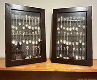 Two wooden framed glass display cases filled with approximately 52 souvenir and commemorative spoons from various locations worldwide.
