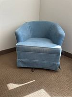 Front angle view of blue upholstered swivel rocking chair with skirted base on carpet.