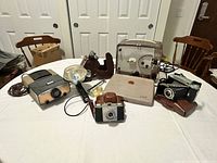 Overview of the lot including Kodak Brownie 500 8mm projector, Kodak Tourist II camera, Kodak Pony 135 camera, Fujica slide projector, several flash accessories and the Brownie wind-up movie camera in poorer condition.