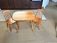 Full view of the child-sized table with two chairs set on carpeted floor, showing 1950s style solid wood construction.