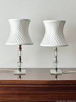 Photo of two small vintage table lamps with rectangular glass and metal bases, wooden accents, and white swirl pattern lampshades on a wooden surface.