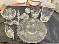 Full view of various glassware and set pieces including small plates, salt and pepper shakers, and a large glass vase, showing the floral etched Cornflower pattern.
