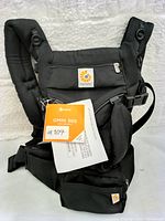 Full frontal image of black Ergobaby Omni 360 baby carrier with tags attached, showcasing the carrier's design and features including padded straps and waist support pocket.