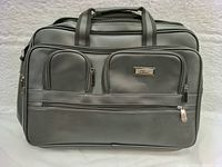 Front view of black leather briefcase showing exterior zippered compartments and GLUCI brand metal plate.