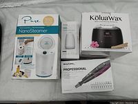 Photo of the four boxed items in the combo kit: Pure NanoSteamer, Beautural Manicure & Pedicure Kit, KoluaWax Waxing Kit, and Homsy Aroma Diffuser.