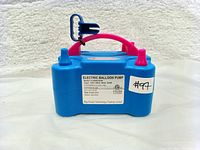 Front view of the electric balloon pump showing Intertek certification label, model number FJY0001USP, and power specifications 120V~60Hz max 600W. Blue body with pink handle and dual nozzle.