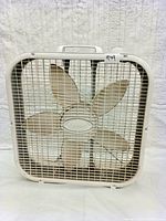 Front view of white Lasko box fan showing white 5-blade fan inside white grille with handle on top.