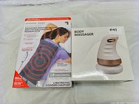 Two boxed items: a Sharper Image Massaging Weighted Heating Pad in original packaging showing product image and features, next to a white box labeled 'Body Massager' showing a massager device image.