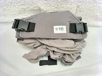 Folded gray fabric baby wrap carrier with black plastic buckle clips on a white textured background.
