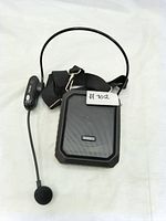 Photo of portable wireless voice amplifier with strap and UHF microphone headset showing handheld speaker device and attached mic with headband and foam windscreen.